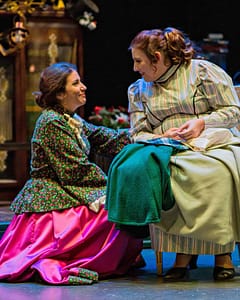 From A Christmas Carol, one actress does cross stitch, another kneels down next to her to chat