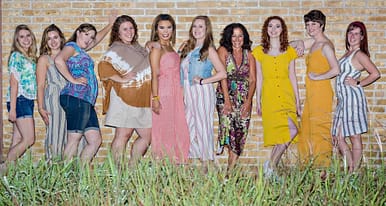10 girls pose standing in a line against a brick wall